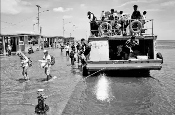  ??  ?? Passengers of a boat walk through rising sea water during high tide at Kali Adem port in Jakarta. — Reuters photos