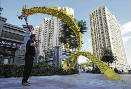  ?? NG HAN GUAN/ASSOCIATED PRESS ?? A resident wields a cloth dragon Tuesday outside the Evergrande Yujing Bay residentia­l complex in Beijing, China. Global investors are watching nervously as one of China’s biggest real estate developers struggles to avoid defaulting on tens of billions of dollars of debt, fueling fears of possible wider shock waves for the financial system.