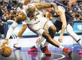  ?? LM Otero Associated Press ?? THE LAKERS’ LeBron James reaches for the ball while he battles Dallas’ Luka Doncic on Sunday. James suffered a right foot injury in the comeback win.