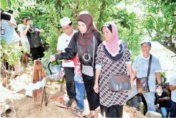  ??  ?? Nadin Junianti Najiri pouring scented water on her late husband’s grave after the burial yesterday.