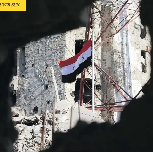  ?? MOHAMAD ABAZEED / AFP / GETTY IMAGES ?? The Syrian national flag stands amid shattered buildings in Daraa-al-Balad on Thursday after Syria’s army entered the area, the cradle of the uprising that sparked the country’s seven-year war, following a deal for rebels to hand over their heavy...