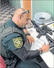  ?? AP PHOTO ?? A Broward County, Florida, Sheriff’s Deputy processes paperwork, to take possession of and destroy an Ar-style firearm owned by Ben Dickmann, a photograph­er in Florida. Dickmann turned in his weapon after the shooting at Marjory Stoneman Douglas High...