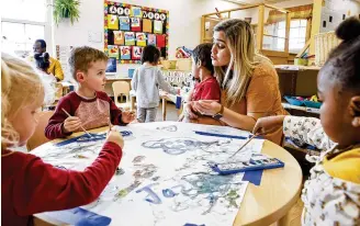  ?? NICK GRAHAM / STAFF ?? Lead teacher Amanda Varner holds student Ridvaan S. while Stephen K. and other students paint in the pre-K class at Mini University child care April 6 on Miami University campus in Oxford.