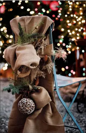  ?? Staff Photo by Dan Henry ?? The perfect accent for the woodland/lodge/natural greens look is burlap. Sue Chamberlai­n used a 3-foot by 9-foot burlap table runner to create a chair cover with double-loop back. She tied fresh greens, berries and pods into the back bow for decoration.
