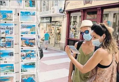  ?? DAVID ARQUIMBAU SINTES / EFE ?? Unos turistas con mascarilla miran postales en Mallorca