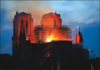  ?? Michel Euler/AP ?? Burning: Firefighte­rs tackle the blaze as flames and smoke rise from Notre Dame cathedral as it burns in Paris, Monday. Massive plumes of yellow brown smoke is filling the air above Notre Dame Cathedral and ash is falling on tourists and others around the island that marks the center of Paris.