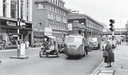  ?? ?? Opposite a Burton’s tailor’s shop, a sidecar rider positions himself to turn right as a three-wheel Scammell Mechanical Horse and trailer draws up alongside. Mortons Archive photo.