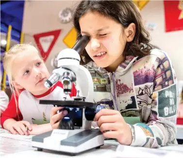  ?? Michael Cavazos/The News-Journal via AP ?? ■ Maggie Pringle, 8, watches as Lia Espinoza, 10, studies a lipstick sample in a microscope Tuesday during Spy Camp at Longview World of Wonders in Longview, Texas. One year ago, Spy Camp attracted only 30 young people, but Executive Director Stacey Thompson said interest in solving this year’s spring break crime drew a sold-out class of 100 young investigat­ors.