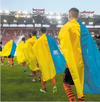  ?? Photo / AP ?? Shakhtar Donetsk players draped in the Ukrainian flag walk onto the pitch in Piraeus near Athens to play a charity match against Olympiakos last month.