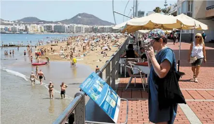  ?? reuters ?? Too many people: a tourist reading an informatio­n panel on the edge of the crowded las Canteras Beach in las palmas de Gran Canaria, spain. Overtouris­m is deemed to be a ‘suicidal growth model’. —