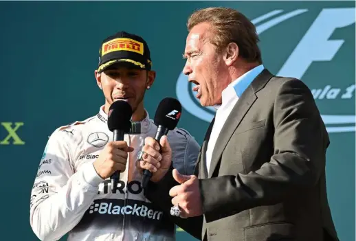  ??  ?? Hamilton speaking on the podium with Hollywood star Arnold Schwarzene­gger after winning the Australian Grand Prix. — AFP