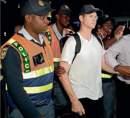  ?? PHOTO: AP ?? South African police escort Steve Smith through OR Tambo Internatio­nal Airport, Johannesbu­rg after the Australian cricket captain was sent home.