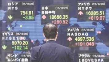  ?? — Reuters ?? A man looks at an electronic board showing the stock market indices of countries outside a brokerage in Tokyo.