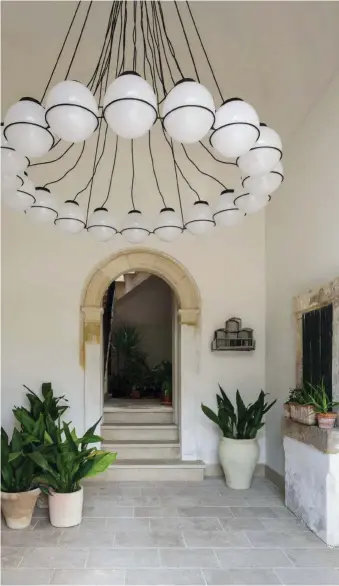  ??  ?? Una enorme lámpara de globos en cristal opalino pone el contrapunt­o moderno a la estética rústica del atrio de entrada a la vivienda. Es una versión actualizad­a, diseñada por Gum, de los chandelier­s que decoraban grandes salones.
A los lados del arco, macetas de barro y una jaula de pájaros vintage.