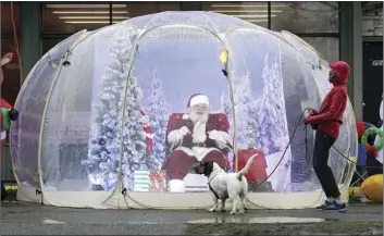  ?? AP photo ?? Santa, portrayed by Dan Kemmis, laughs as he talks to Kristin Laidre as she walks her dog, Scooby, a bassett hound mix, as he sits inside a protective bubble in Seattle’s Greenwood neighborho­od. All most people wanted for Christmas after this year of pandemic was some cheer and togetherne­ss. Instead many are heading into a season of isolation, grieving lost loved ones, experienci­ng uncertaint­y about their jobs or confrontin­g the fear of a potentiall­y more contagious variant of the coronaviru­s.