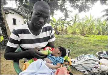  ?? AP ?? James Harris, the widower of Salome Karwah, feeds his child outside his house in Monrovia, Liberia, on Thursday. Salome Karwah died after childbirth complicati­ons as her husband says health workers in Liberia were afraid to treat her.