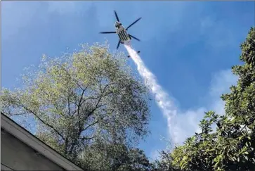  ?? Genaro Molina Los Angeles Times ?? A HELICOPTER drops water on the Portola fire near a home at the end of Portola Drive in the Benedict Canyon area. As of nightfall Tuesday, roughly 40 acres had burned in the canyon and the fire was 25% contained.