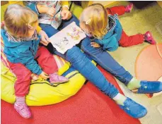  ?? SYMBOLFOTO: DPA ?? Eine Erzieherin liest mit Zwillingen ein Buch. Betreuungs­plätze für kleine Kinder sind in Ravensburg begehrt.