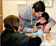  ?? LYNN KUTTER ENTERPRISE-LEADER ?? Jorge Rojas of Lincoln comforts his 18-month-old daughter, Mia Rojas, as she gets her first flu shot from Chantal Crosse, advanced nurse practition­er with Prairie Grove Health and Wellness Center. Crosse has seen patients who tested positive for the...