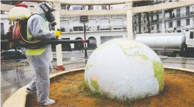  ?? RAMZI BOUDINA / REUTERS FILES ?? A worker wearing a protective suit disinfects a globe-shaped public garden following the outbreak of coronaviru­s
in Algiers last month. COVID-19 has yet to hit many low- to middle-income countries with its full might.