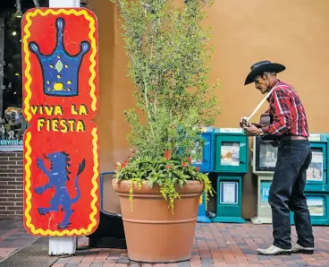  ?? PHOTOS BY GABRIELA CAMPOS/THE NEW MEXICAN ?? Agapito Chavez plays his guitar Thursday for passing tourists next to one of the Fiesta de Santa Fe signs recently hung around the Plaza.