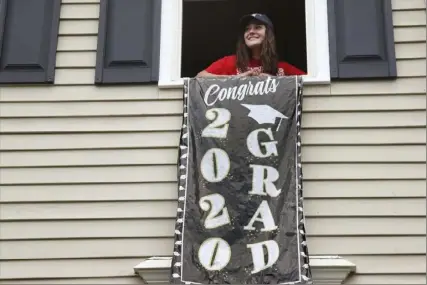  ?? Elise Amendola/Associated Press ?? High school graduate Lizzie Quinlivan looks out over a graduation window banner June 1 at her home in Hingham, Mass. She opted to attend closer-to-home Georgetown University instead of colleges on the West Coast, which were on her original wish-list.