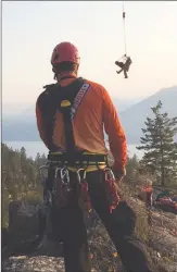  ?? Special to the Herald ?? A specialist in cave rescues descends from a helicopter Monday at Skaha Bluffs as a member of Penticton Search and Rescue looks on.