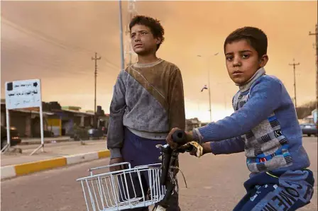  ??  ?? Boys looking on at a street as smoke rises from oil wells set ablaze by IS before the militants fled the oil-producing region of Qayyara. — Reuters