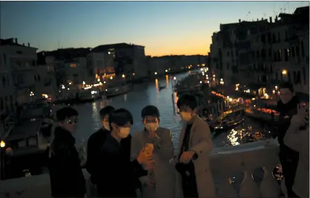  ?? ASSOCIATED PRESS ?? Tourists wearing protective masks pose for a photograph at the Rialto bridge as the sun sets in Venice, Italy, Friday, Feb. 28. Authoritie­s in Italy decided to re-open schools and museums in some of the areas less hard-hit by the coronaviru­s outbreak in the country which has the most cases outside of Asia, as Italians on Friday yearned for a return to normal life even amid fears that the outbreak could plunge the country’s economy into recession.