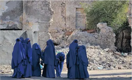  ??  ?? FEW OPTIONS: Schoolgirl­s walk past the ruins of the old colonial post office in Kismayo. The only schools in this city are private, and therefore prohibitiv­ely expensive for most impoverish­ed returnees.