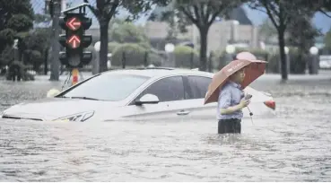  ??  ?? 0 A man wading past a submerged car along a flooded street following heavy rains in Zhengzhou