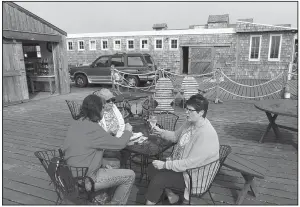  ??  ?? Visitors share a seafood snack on the deck at Oystervill­e Sea Farms, where oysters can be bought ready to eat or to take home.