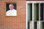  ??  ?? A portrait of St. John Paul II hangs beside a row of empty lockers in the main hallway of Quigley Catholic High School.