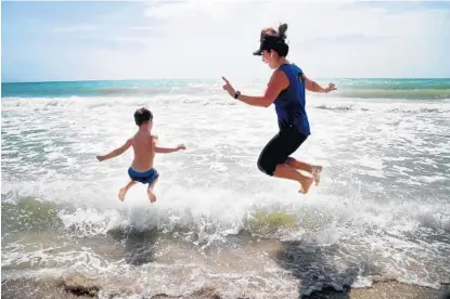  ?? SUSAN STOCKER/SOUTH FLORIDA SUN SENTINEL ?? Duygu Walter, right, and her son Dylan, 4, of Sunny Isles Beach, jump into the ocean in Hollywood as beaches reopened Tuesday. “I’m glad they’re opening the beaches. It gives me hope,” Walter said. Broward’s opening follows Palm Beach County’s reopening last week.