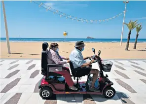  ??  ?? A couple wearing face masks ride a scooter along the boardwalk of the closed Levante Beach in Benidorm, Spain, at the start of the month