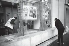  ?? Christophe Ena/Associated Press ?? ■ A worker clears debris in a bank Sunday as a man watches through smashed windows in Paris. Paris monuments reopened, cleanup workers cleared debris and shop owners tried to put the city on its feet again Sunday after running battles between yellow-vested protesters and riot police left 71 injured and caused widespread damage to the French capital.