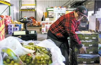  ?? Gabrielle Lurie / The Chronicle ?? Top: At S.F.’s Wholesale Produce Market, Carolyn Lasar (right) hands a box of donated greens to Ebony Wilkerson of Catholic Charities. Above: Organizing donated fruit at the market.