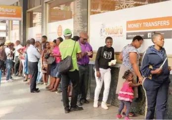  ??  ?? People queue to withdraw US dollars from a money transfer shop in Harare, Zimbabwe. — Reuters