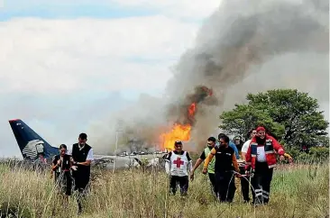  ?? AP ?? Rescue workers carry an injured person on a stretcher, right, as airline workers, left, walk away from the site where an Aeromexico airliner crashed in a field near the airport in Durango.