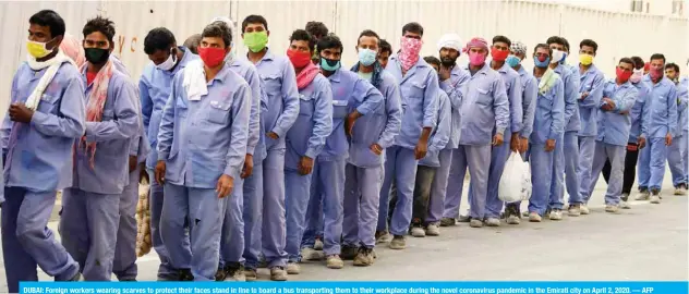  ?? — AFP ?? DUBAI: Foreign workers wearing scarves to protect their faces stand in line to board a bus transporti­ng them to their workplace during the novel coronaviru­s pandemic in the Emirati city on April 2, 2020.