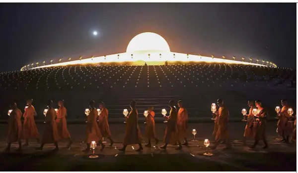  ??  ?? Lighting the way: Buddhist monks carrying lit candles while the full moon rises during prayers to mark Makha Bucha Day at the Wat Phra Dhammakaya temple, near Bangkok. — AFP