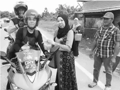  ??  ?? Zuraida gives away packs of ‘bubur pedas’ to motorcycli­sts passing Kampung Semarang.