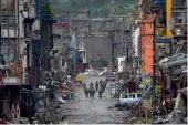  ?? — AFP ?? Soldiers walk past destroyed buildings in Bangolo district in Marawi, Philippine­s, on Tuesday.