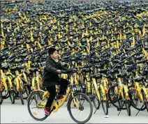  ?? GUO QI / FOR CHINA DAILY ?? An Ofo customer rides past piles of the company’s bikes in Xiangyang, Hubei province.