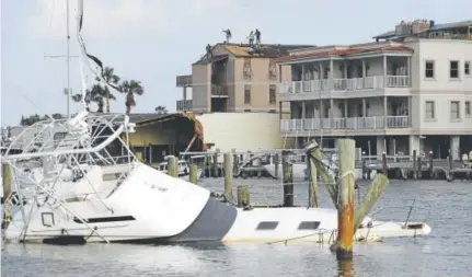  ?? Eric Gay, The Associated Press ?? Workers repair a roof in the distance as a partially submerged boat rests in the Port Aransas Marina in south Texas.