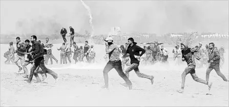  ?? ADEL HANA
THE ASSOCIATED PRESS ?? Palestinia­n protesters run for cover from teargas fired by Israeli troops near the border fence, east of Khan Younis, in the Gaza Strip, Tuesday.