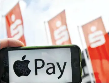  ?? FOTO: DPA ?? Smartphone mit Apple-Pay-Logo vor Sparkassen­fahnen: Experten prophezeie­n, dass die Verbindung des Bezahldien­stes mit der Girocard dem mobilen Bezahlen einen deutlichen Schub verleihen könnte.