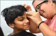  ??  ?? Ash Thiagaraja­n, 10, gets a lightning scar tattoo applied to his forehead by Kassandra Ayala Tuesday, July 31, during the Harry Potter birthday celebratio­n at the Portervill­e Public Library.