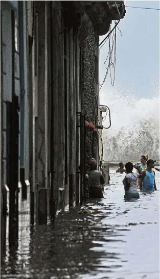  ??  ?? Storm damage: Cubans wading through a flooded street in Havana, after