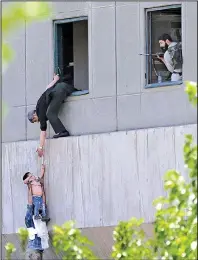  ?? AP/Fars News Agency/OMID VAHABZADEH ?? A man hands a child down to a security guard Wednesday at Iran’s parliament building in Tehran after suicide bombers and gunmen stormed that building and the tomb of Ayatollah Ruhollah Khomeini.